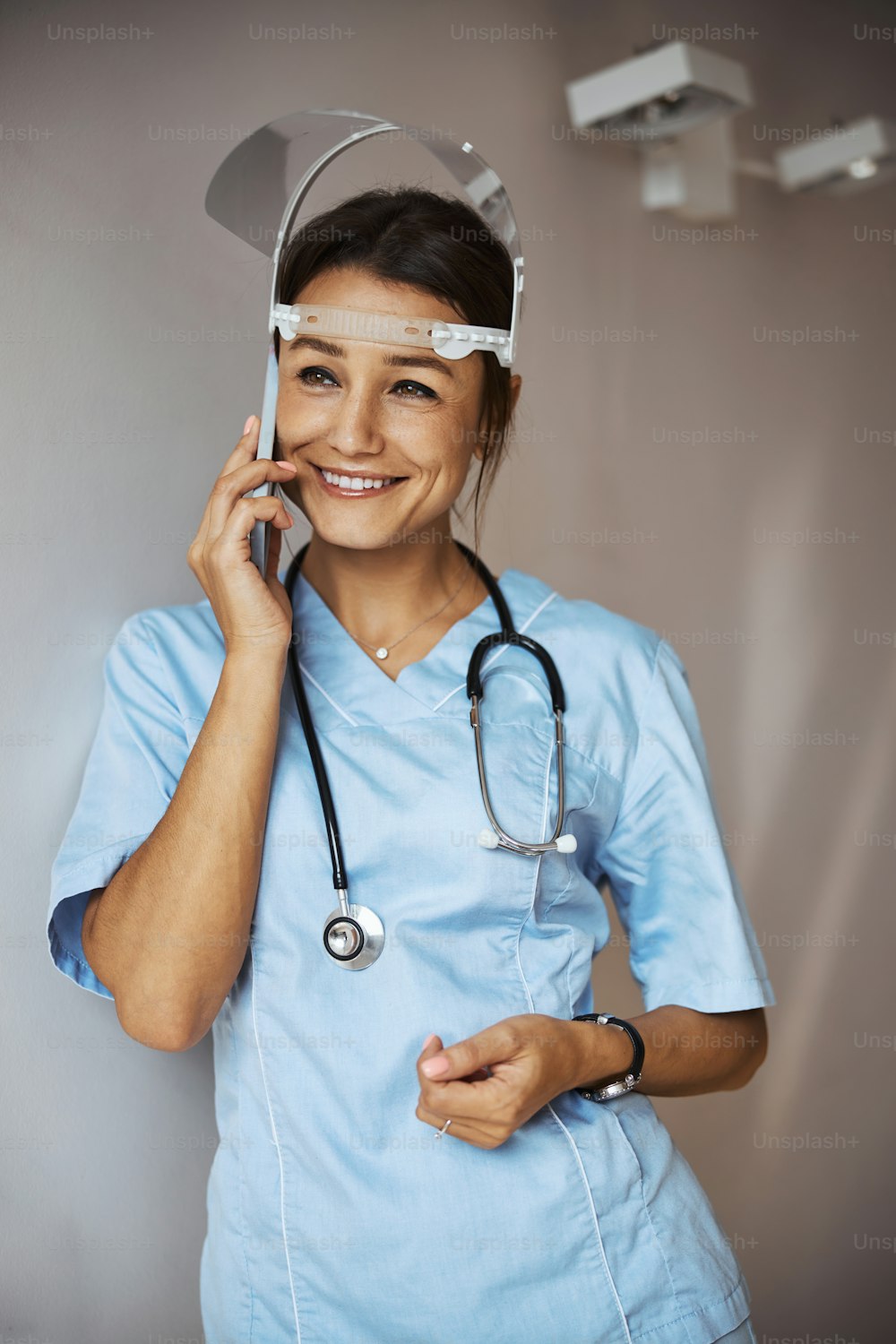 Charming young woman physician wearing protective face mask and medical uniform while having phone conversation and smiling