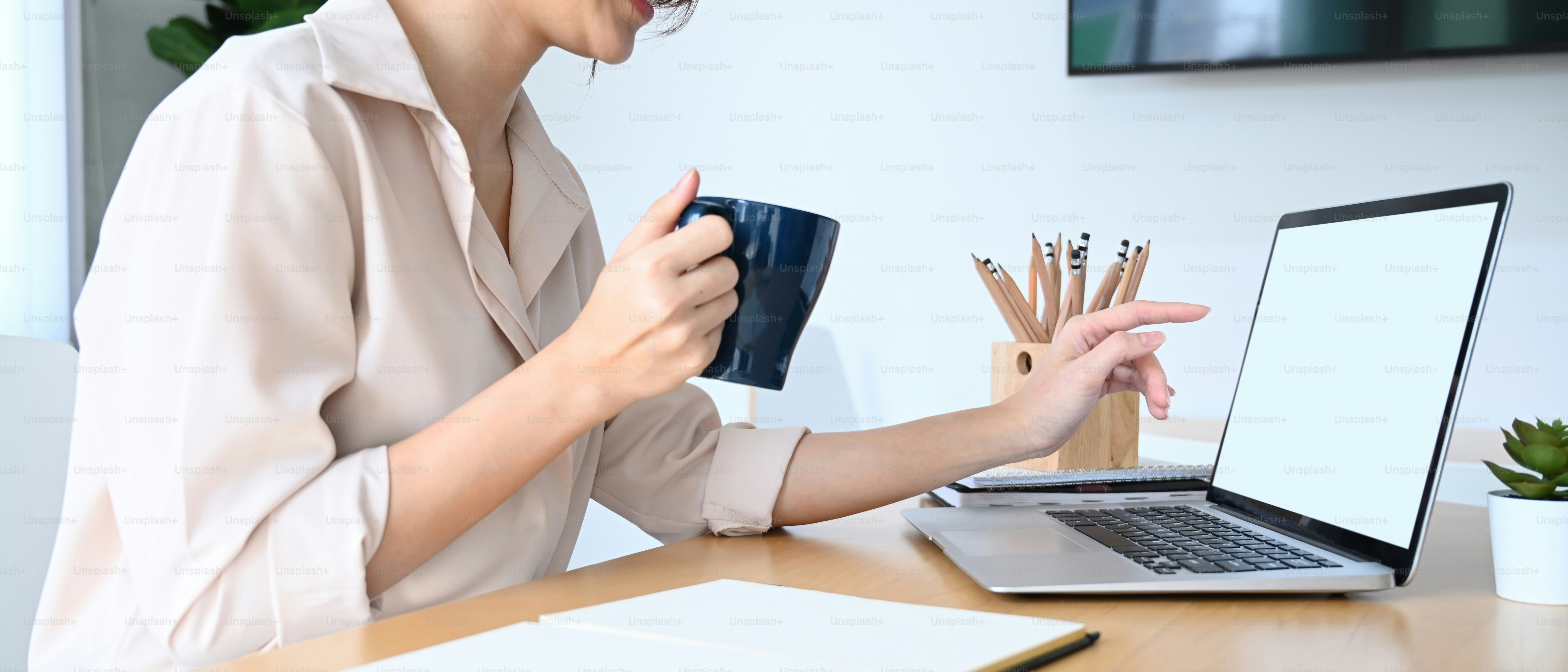 Colpo ritagliato di donna d'affari che tiene una tazza di caffè e indica lo schermo del computer portatile.