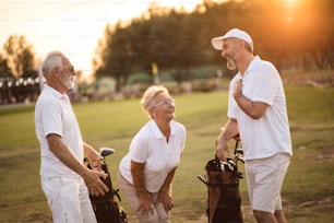 Three smiling seniors golfers talking on golf field.