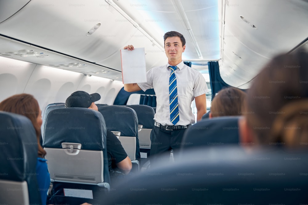 Waist up portrait of air steward explaining the safety procedures to passengers on a commercial airliner before departure
