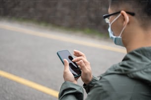 Il giovane uomo zaino in spalla sta viaggiando da solo e usando lo smartphone per trovare un modo con l'uso della maschera, occhiali.