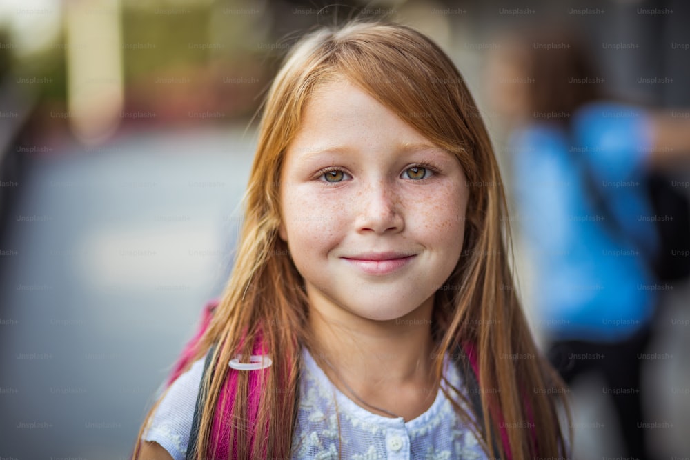 Portrait d’une fille joyeuse aux cheveux roux souriant vers la caméra. La mise au point se fait sur le premier plan.