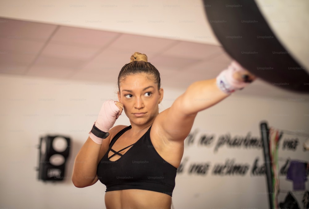 One woman, strong young lady, punching a  bag in gym alone. Focus is on woman.  alone. Focus is on woman.