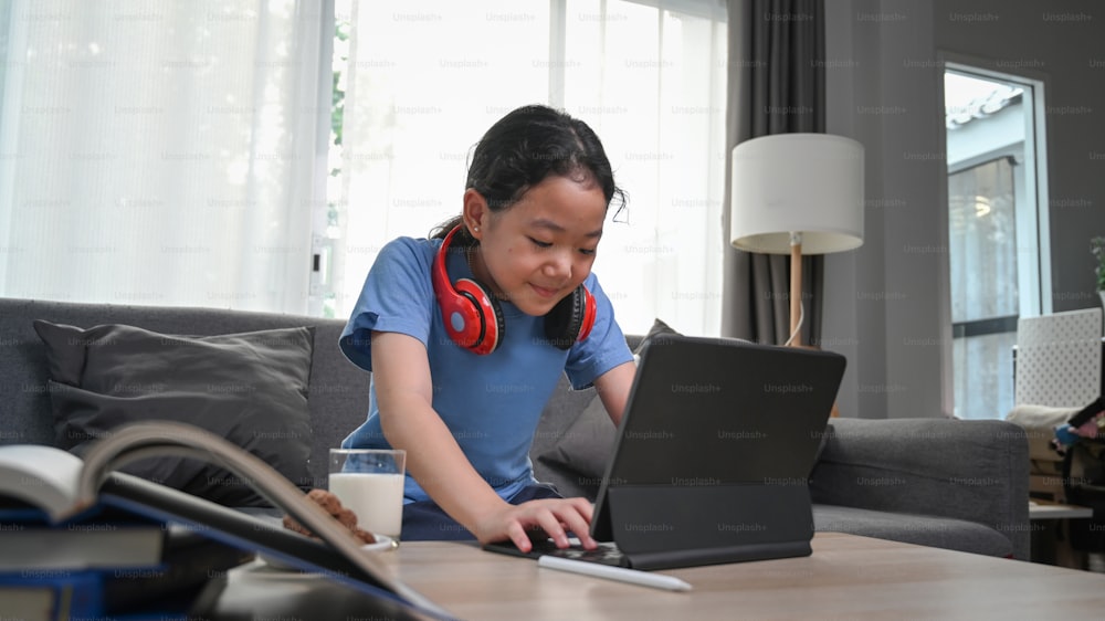 Chica asiática feliz viendo dibujos animados en línea en tableta digital mientras está sentada en el sofá.