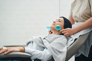 Cliente de salón de belleza joven y atractivo satisfecho que yace en el sillón durante el procedimiento de estiramiento de la piel