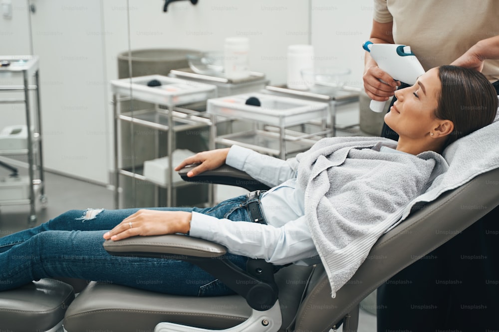 Side view of a beauty salon customer sitting with her eyes closed in the recliner during the cosmetic procedure