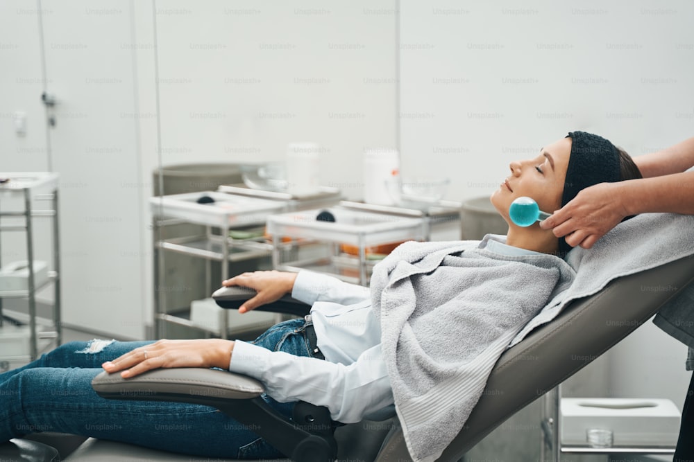 Side view of a Caucasian female patient lying in the armchair during the beauty procedure