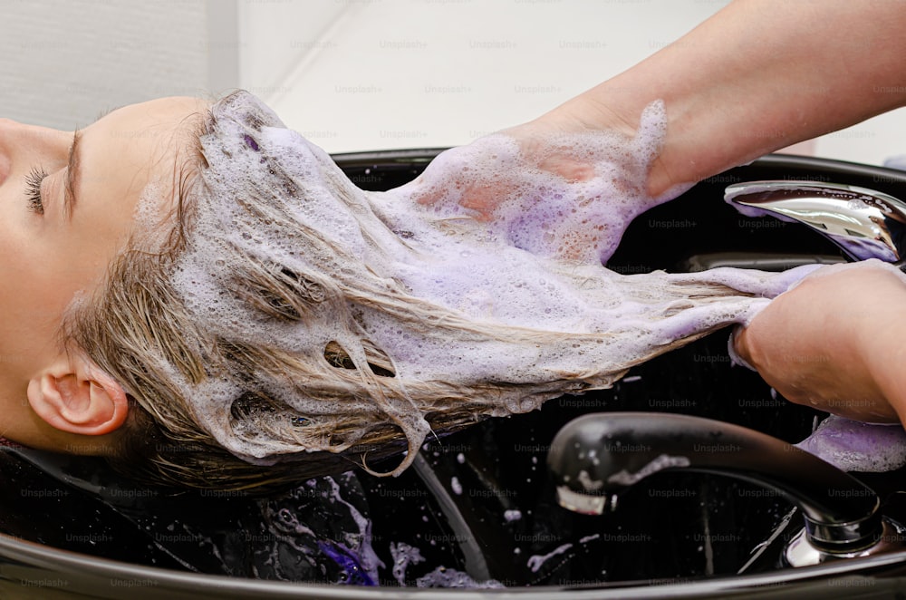 Hair stylist washing hair with no yellow shampoo after hair dyeing.