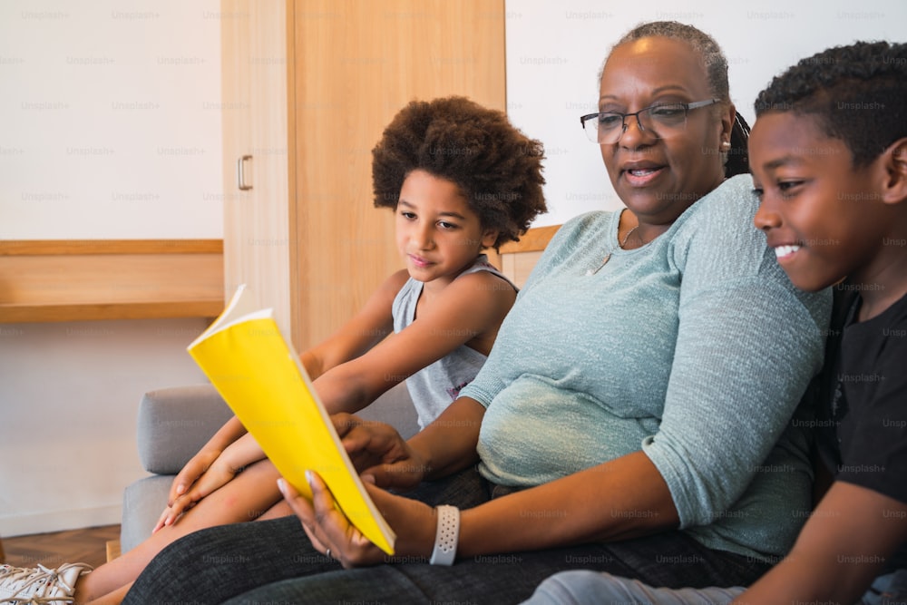 Retrato de una abuela afroamericana leyendo un libro a sus nietos en casa. Concepto de familia.