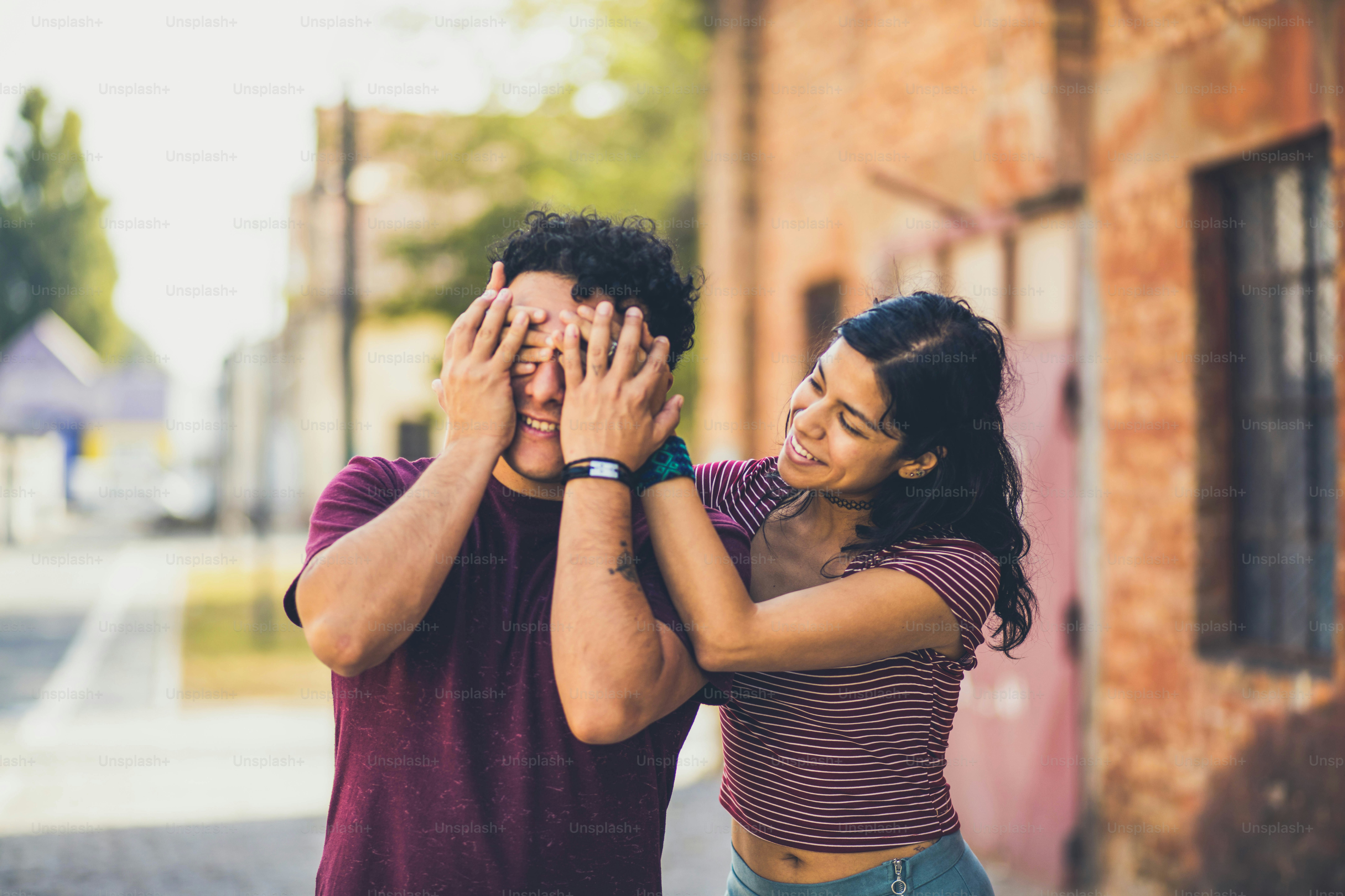 Young couple on the street. Girl holding hands on eyes to her boyfriend.