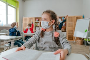 Une élève de l’école primaire portant un masque de protection étudie à l’école pendant la pandémie de COVID-19. Concept de distanciation sociale. Nouveau concept d’éducation normale. Mise au point sélective.