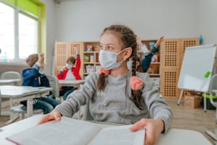 Girl elementary school student in protective face mask studying in the school during COVID-19 pandemic. Social distance concept. New normal education concept. Selective focus.