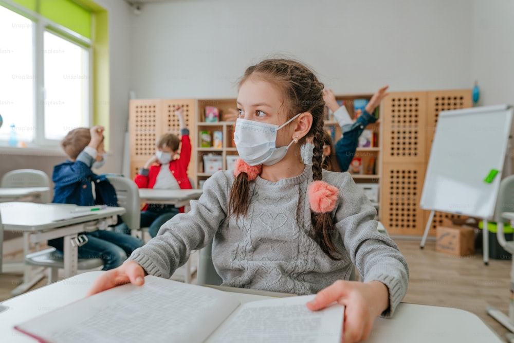 Girl elementary school student in protective face mask studying in the school during COVID-19 pandemic. Social distance concept. New normal education concept. Selective focus.