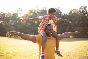 African American father and son in nature. Father carrying his son on shoulders.