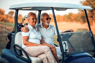 Una pareja de ancianos que juegan al golf monta en un carrito de golf.
