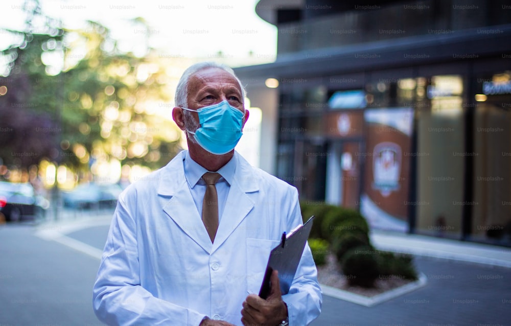 Mature serious doctor on street wearing protective mask.