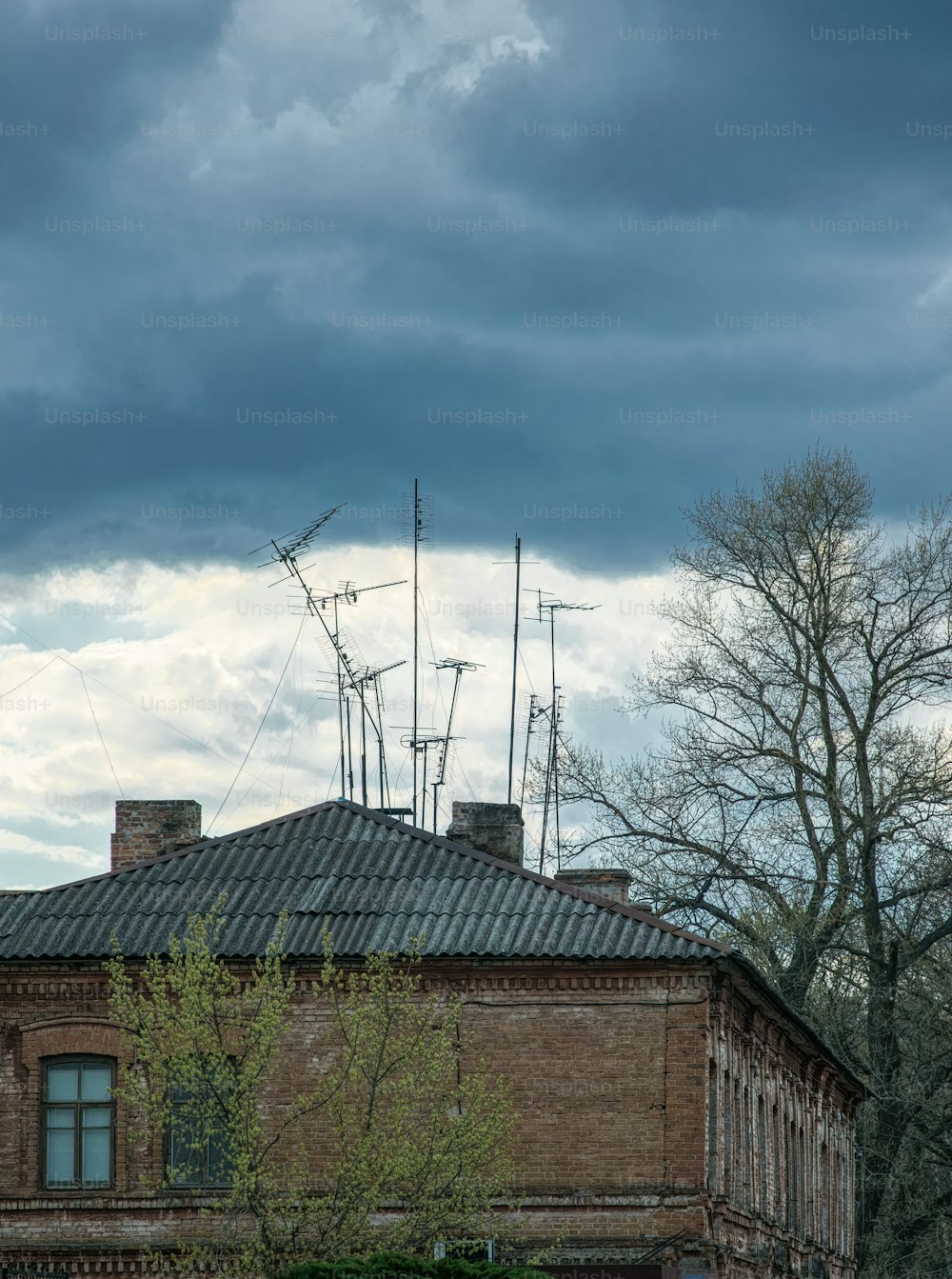時代遅れのアナログ技術と古い老朽化した建築。嵐の空の灰色の雲を背景にしたスレート屋根と古い錆びたテレビアンテナ