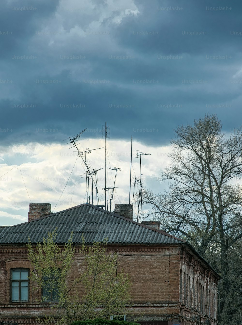 Outdated analog technology and old decrepit architecture. Slate roof and old rusty TV antennas against the backdrop of gray clouds of stormy sky