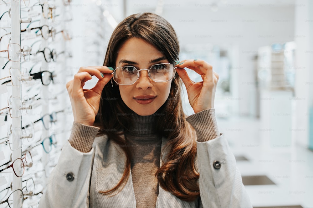 Beautiful and fashionable woman choosing eyeglasses frame in modern optical store.