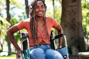 Donna afroamericana su una sedia a rotelle che sorride e ascolta musica con le cuffie al parco.