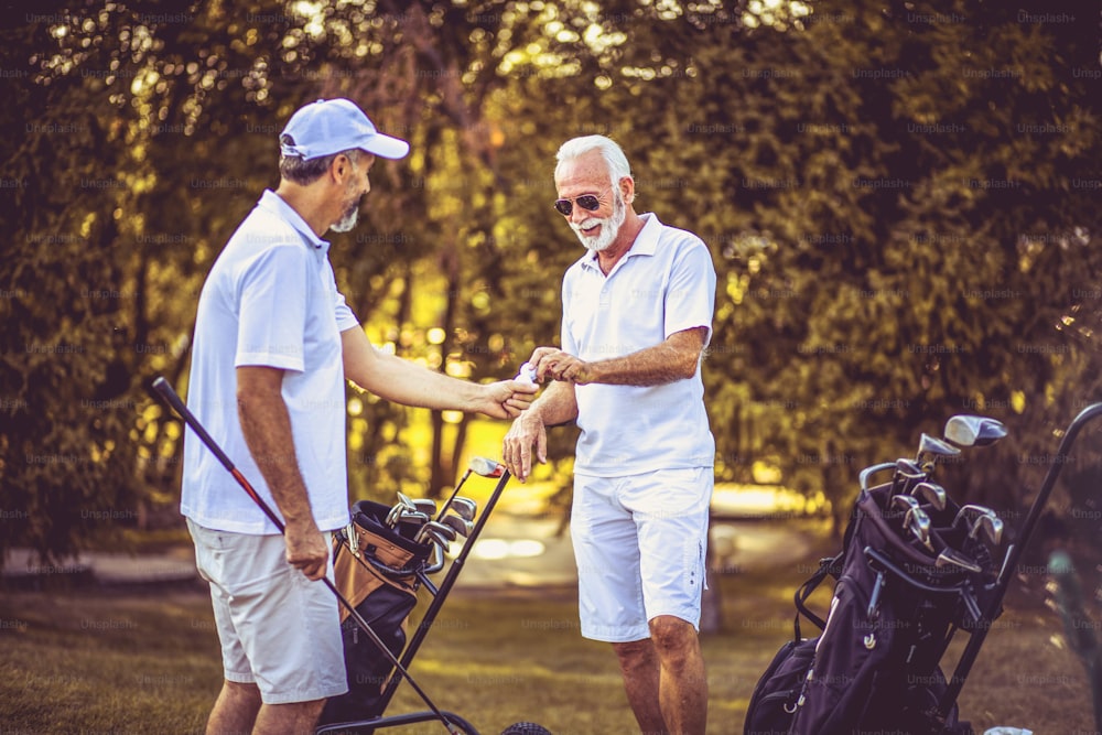 Two older men stand on a golf course and talk. Focus is on background.