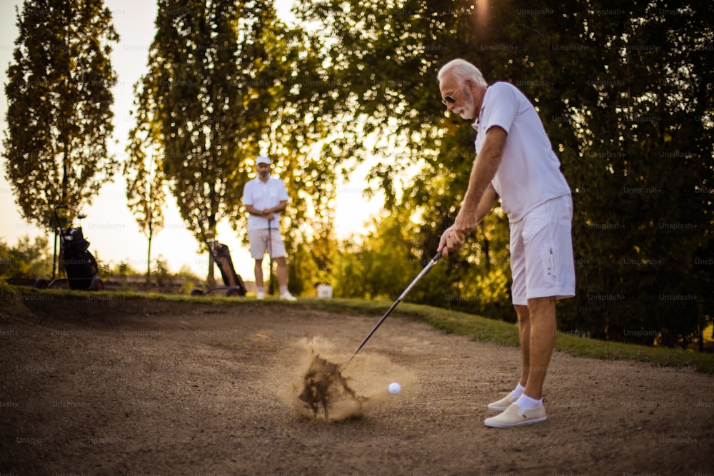 Two men on the golf course. Man hits a golf ball.