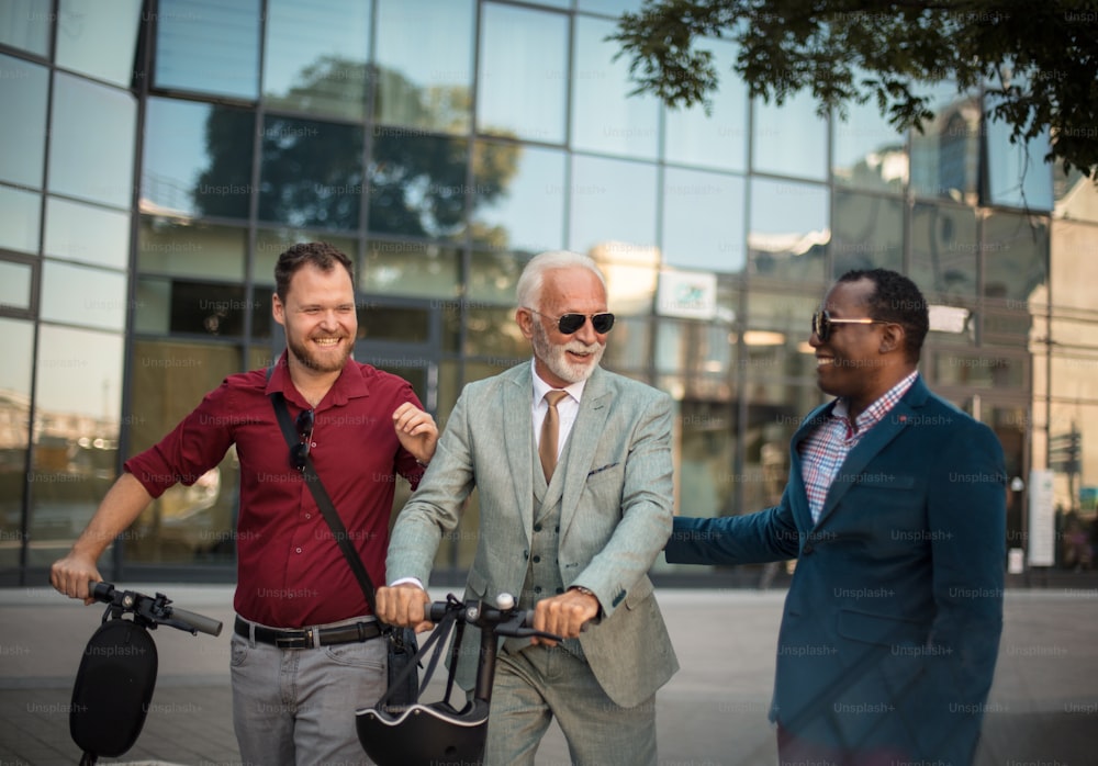 Três homens de negócios na rua. Dois homens com scooter elétrico.