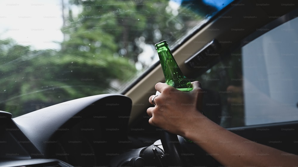 Uomo alla guida di un'auto con una bottiglia di birra. Non bere e guidare il concetto.