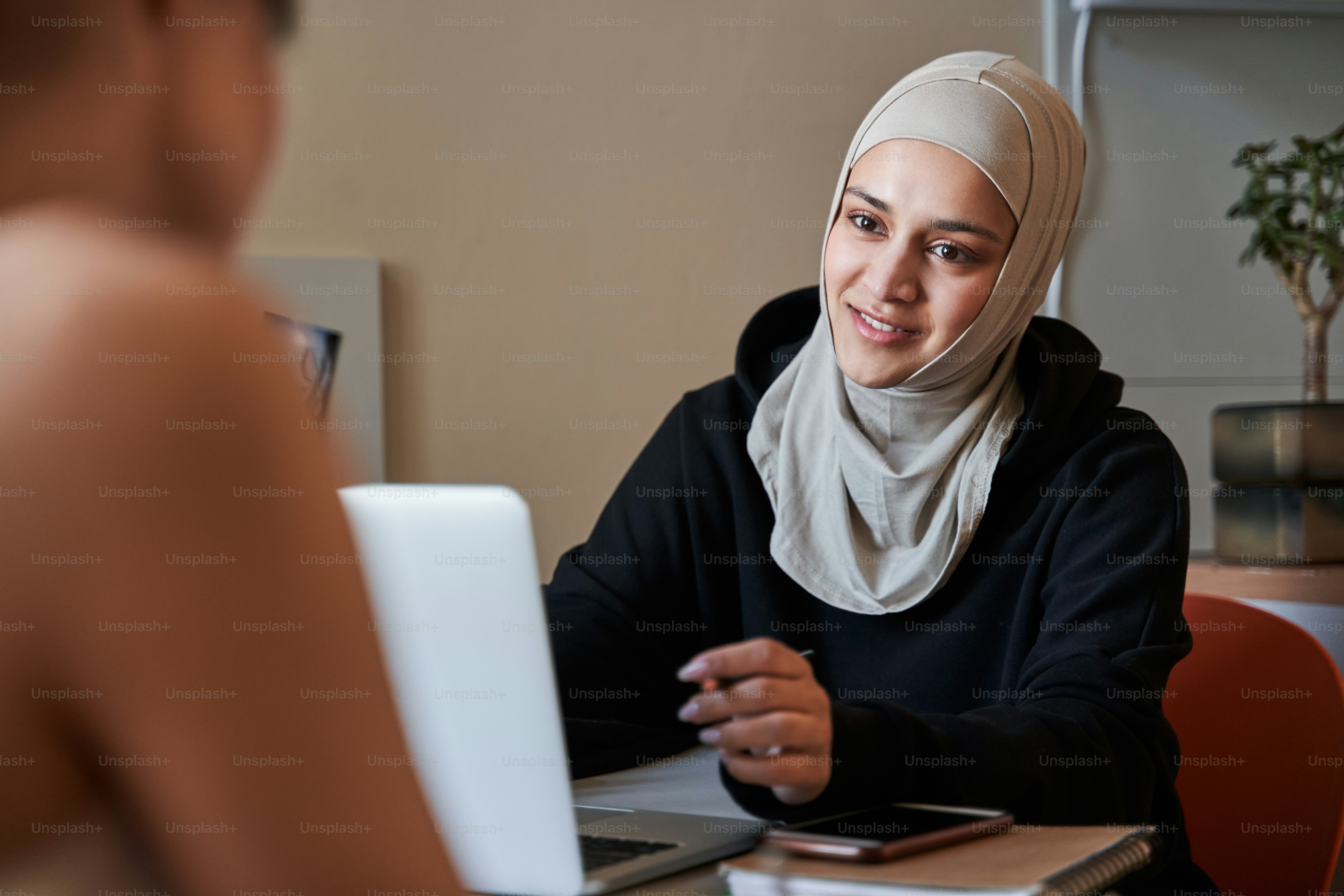 Portrait view of the attractive muslim girl wearing hijab smiling with pleasure while looking at her best friend at home. Stock photo