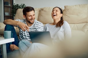 Glückliches Paar lacht und hat Spaß beim Surfen im Internet auf dem Laptop zu Hause.