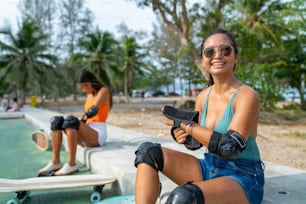 Asiatische Frau mit Freundinnen, die Sicherheits-Skateboard-Handschuhe zum Skaten im Skatepark tragen. Glückliche weibliche Freundschaft genieße den Sommer Outdoor Active Lifestyle Spiele Extremsport Surf Skate zusammen