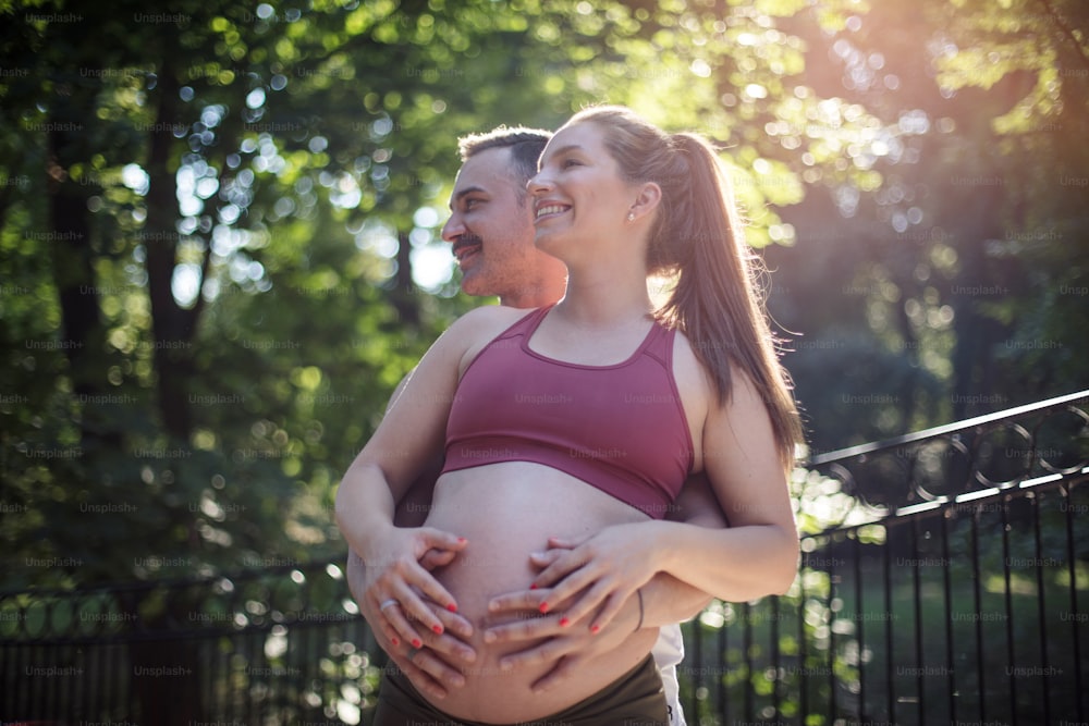 Sports couple standing in the park and touch the stomach.