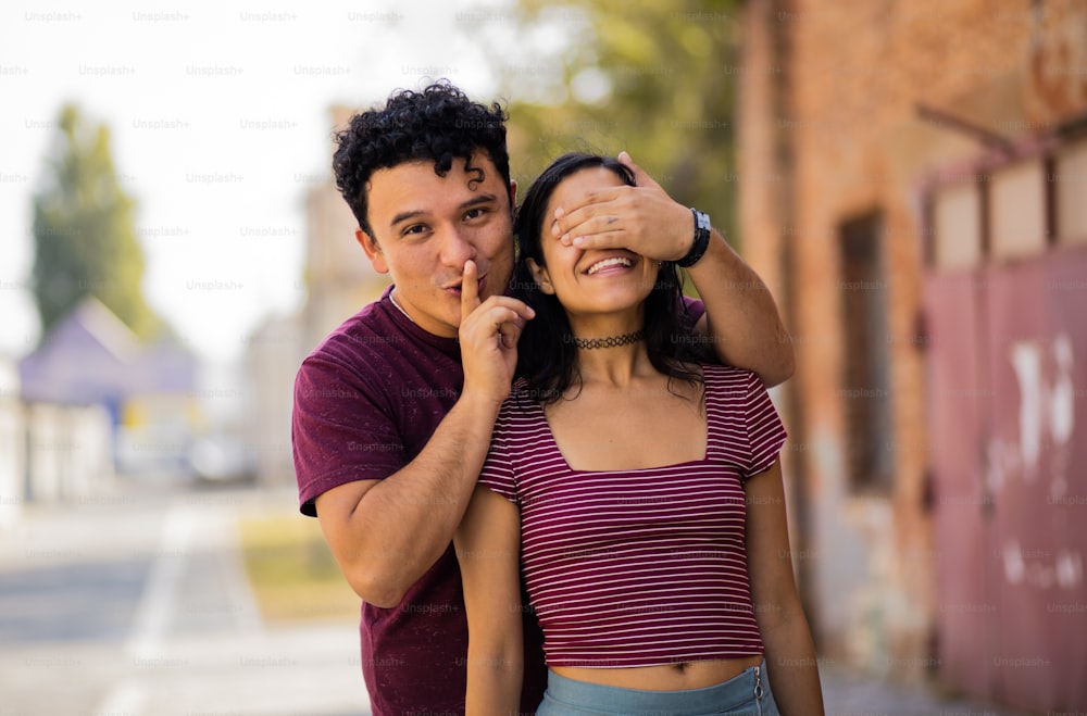 Young couple on the street. Boyfriend holding hands on eyes his girlfriend.