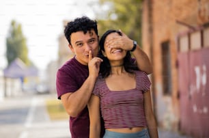 Young couple on the street. Boyfriend holding hands on eyes his girlfriend.