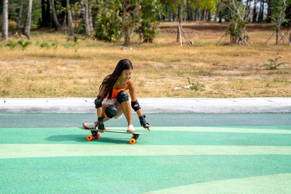 해변 옆 스케이트보드 공원에서 안전 스케이트보드 무릎 패드 스케이트를 탄 매력적인 아시아 여성. 행복한 여성은 공공 공원에서 여름 야외 활동적인 라이프 스타일을 즐기며 익스트림 스포츠 서핑 스케이트를 즐깁니다.