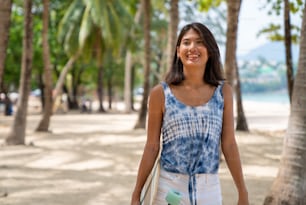Retrato da mulher asiática sorridente atraente segurando skate andando na praia no dia ensolarado do verão. Confiança feminina desfrutar e ter divertido estilo de vida de atividade ao ar livre e esportes radicais surf skate