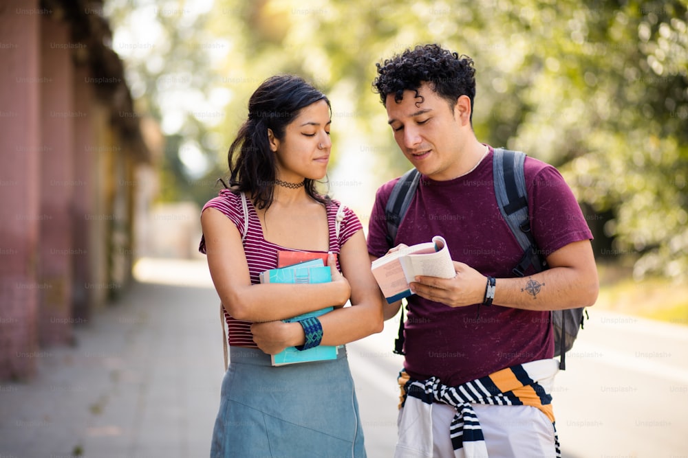Zwei junge Studenten stehen mit Büchern auf der Straße und unterhalten sich.