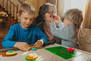 Grand-mère jouant avec ses petits-enfants avec des enfants jouant à l’argile à l’intérieur. Mise au point sélective.