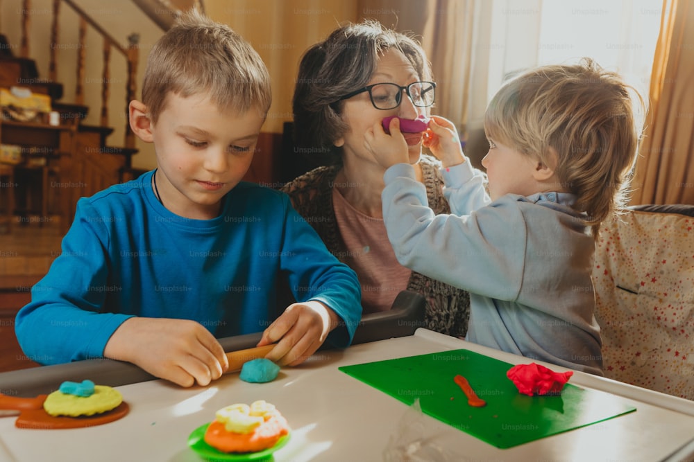 Grandmother playing with her grandchildren with kids play clay indoor. Selective focus.