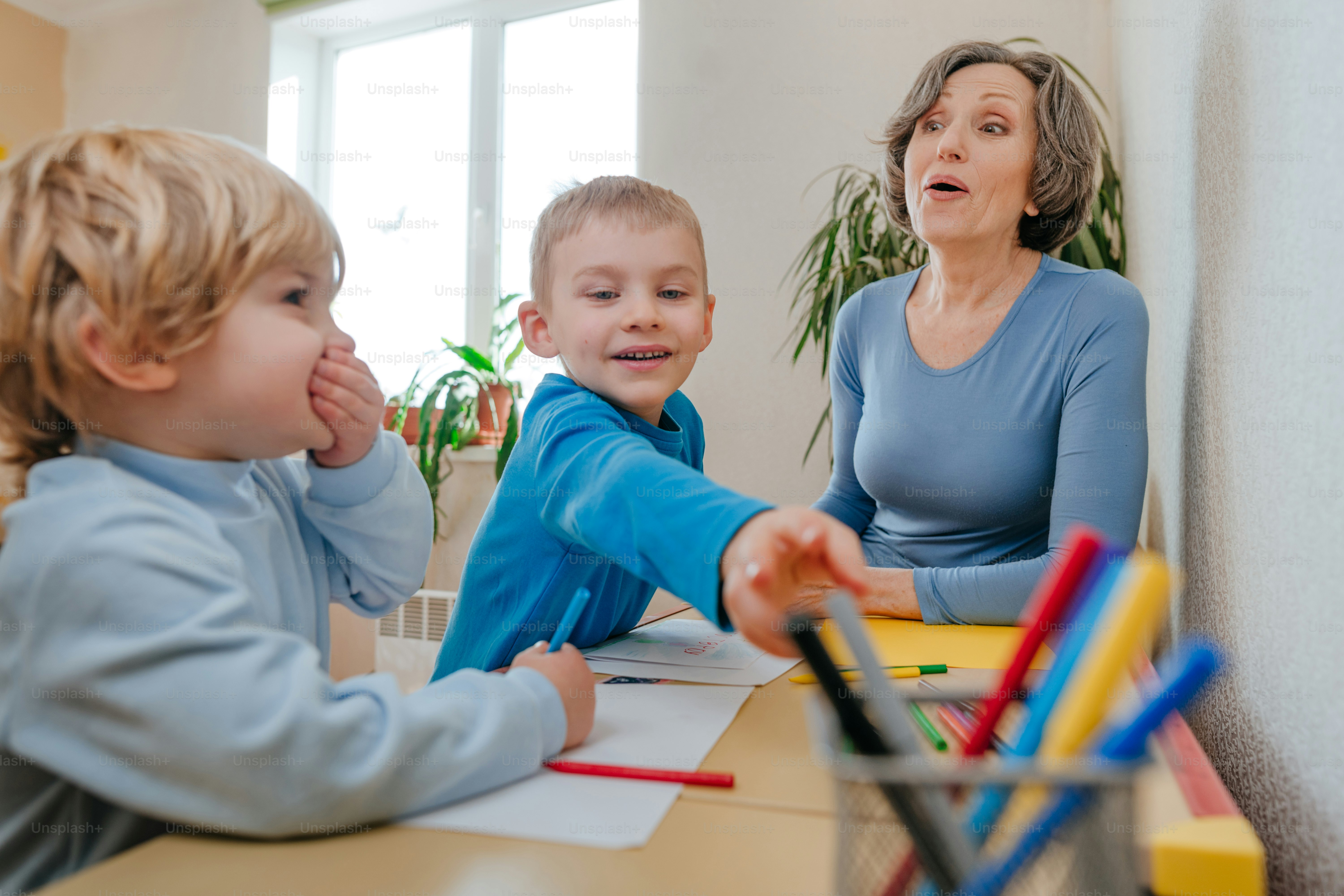 Grand-mère dessinant avec ses petits-enfants assis à la table à l’intérieur. Mise au point sélective.