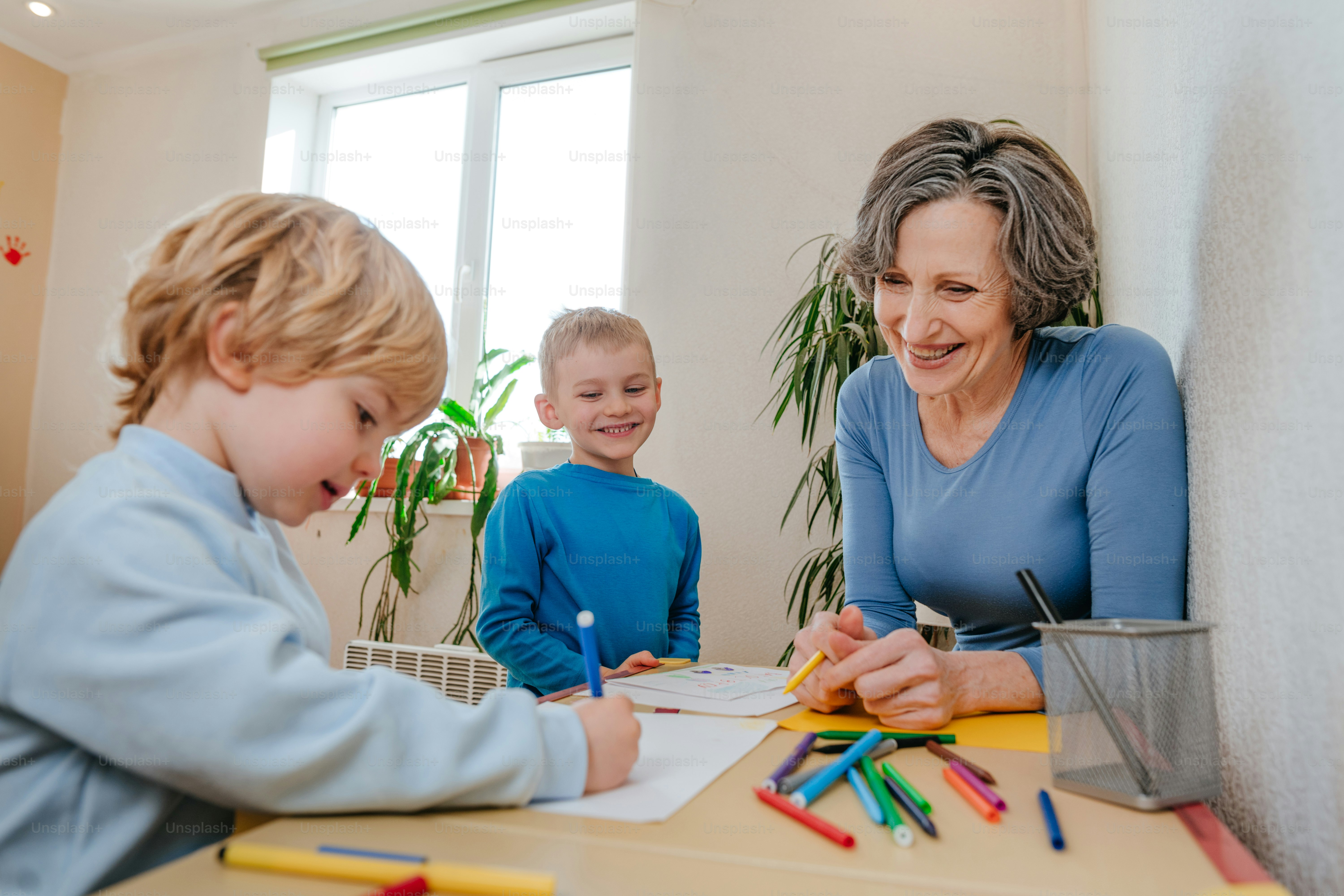 Grand-mère dessinant avec ses petits-enfants assis à la table à l’intérieur. Mise au point sélective.