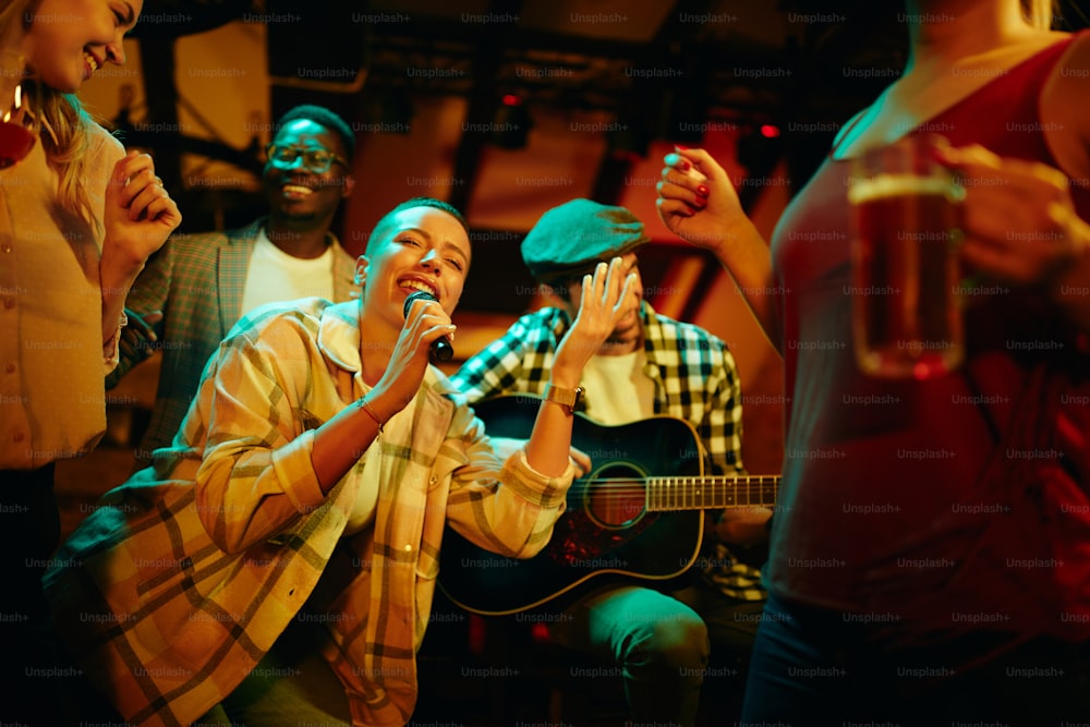 Gruppo di amici che si divertono a una festa al bar di notte. L'attenzione si concentra sulla donna nera che tiene il microfono e canta.