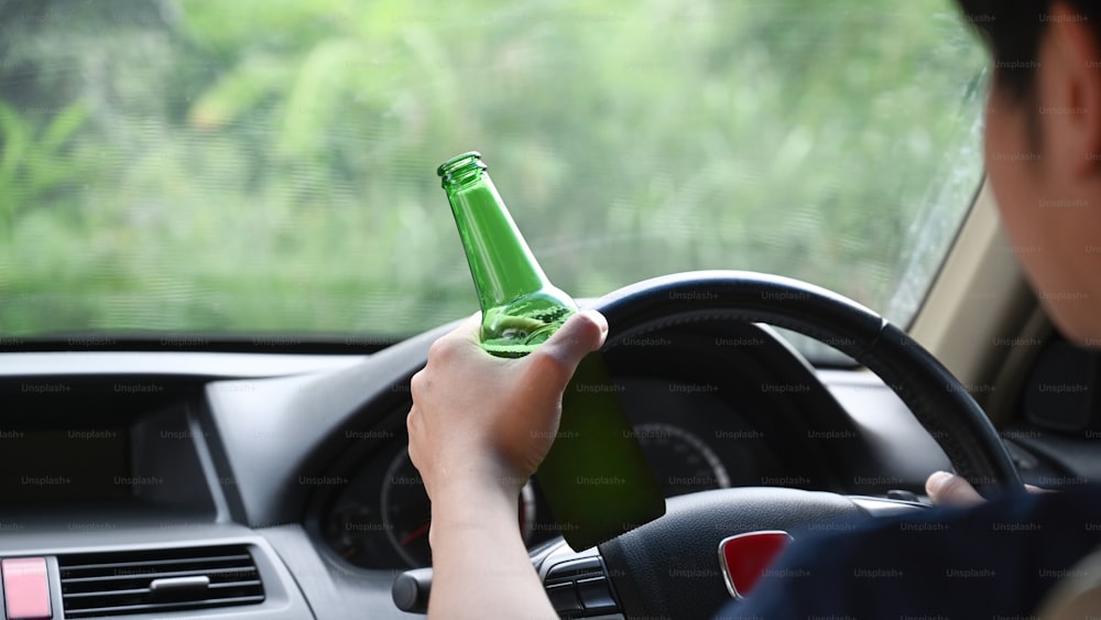Mann fährt ein Auto, während er eine Flasche Bier in der Hand hält. Fahren unter Alkoholeinfluss.