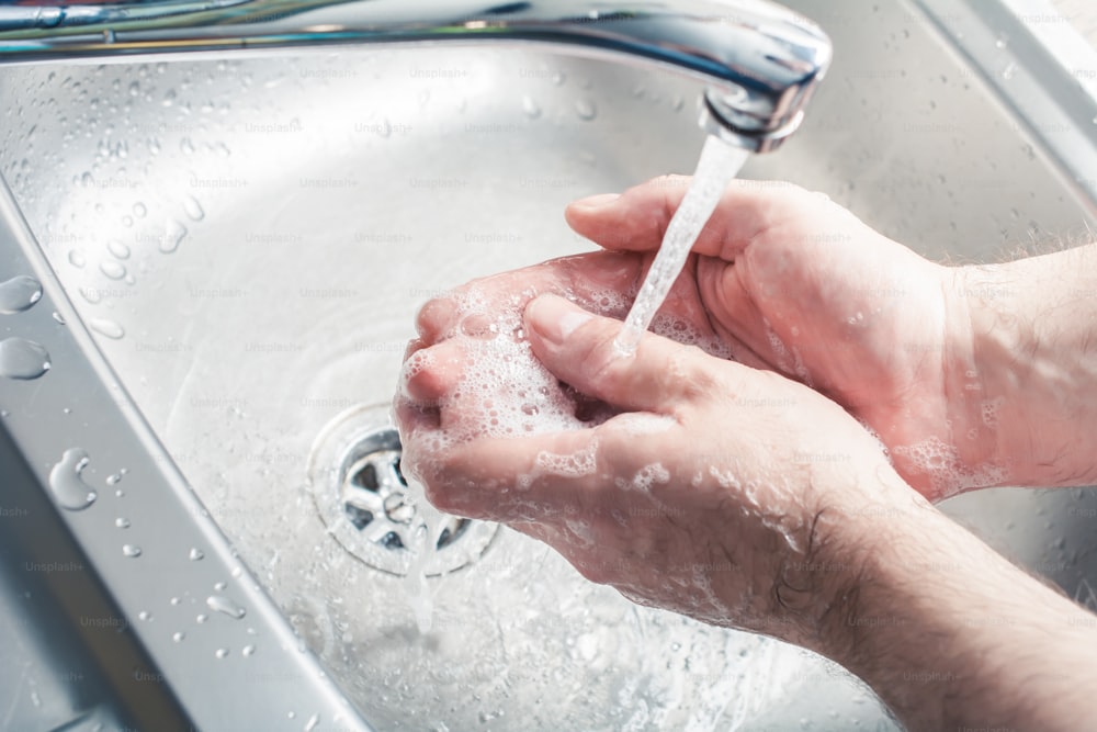 Lavagem masculina mãos ensaboadas sob o fluxo de água na pia da cozinha