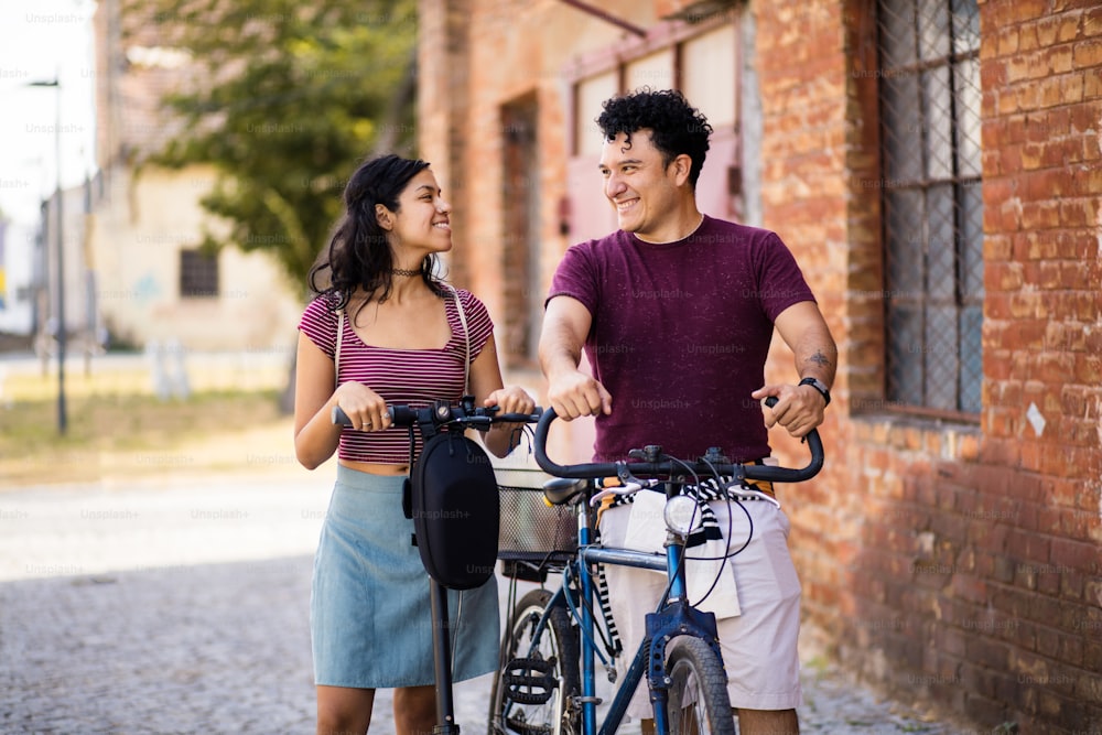 자전거와 전기 스��쿠터를 탄 거리에 있는 젊은 커플.