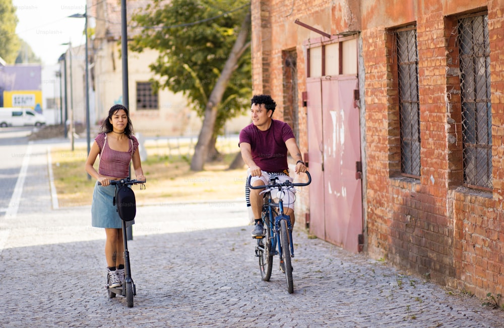 Pareja joven en la calle con bicicleta y patinete eléctrico.