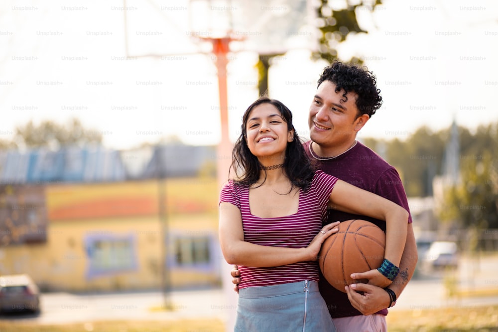 Young couple standing basketball court and holding ball.