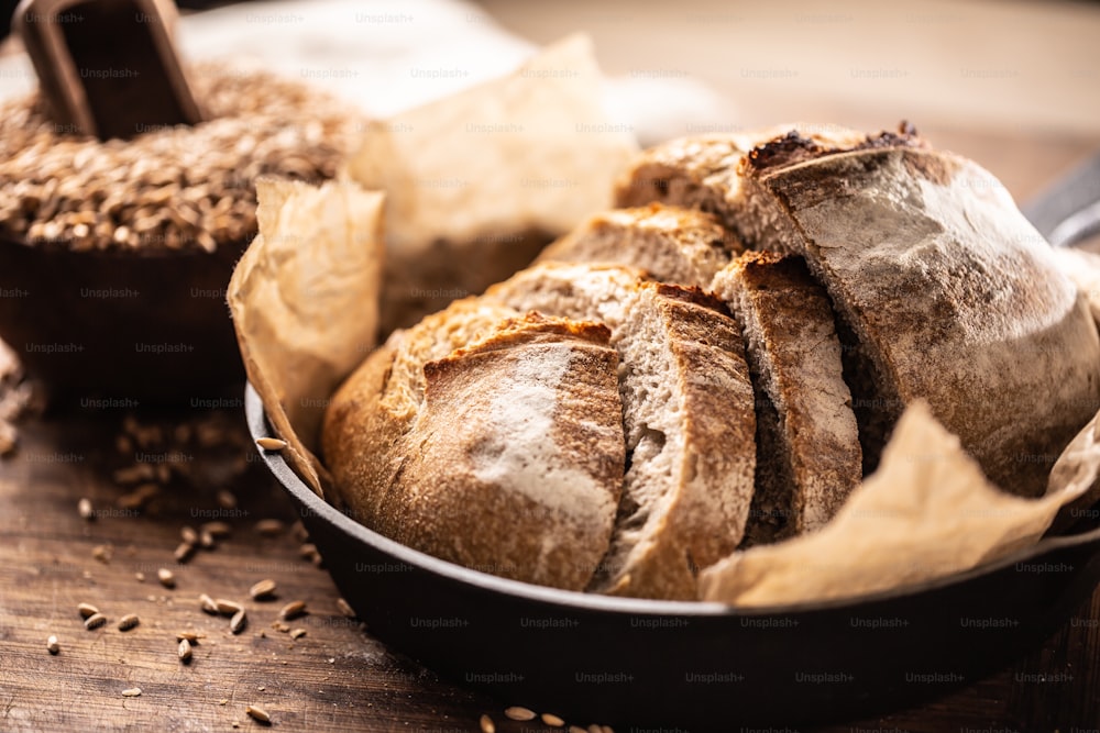 Deliciosas rebanadas de pan de levadura crujientes servidas sobre papel de hornear en la sartén rústica de aleación sobre la mesa de madera con granos de trigo integral en el fondo.