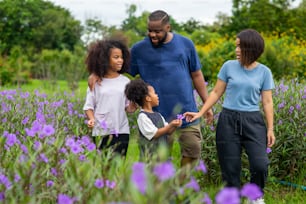 Happy mixed race family in park. African father and Asian mother with two little daughter holding hands walking together in garden. Mom and dad with child girl kid enjoy and having fun in outdoor lifestyle activity.