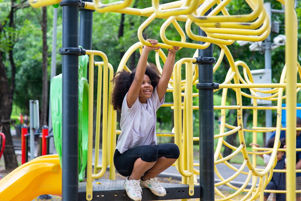 Happy mixed race family in park. Adorable child girl kid playing and hanging on jungle gym at children playground in public park. Smiling little daughter enjoy and having fun outdoor lifestyle weekend activity in summer
